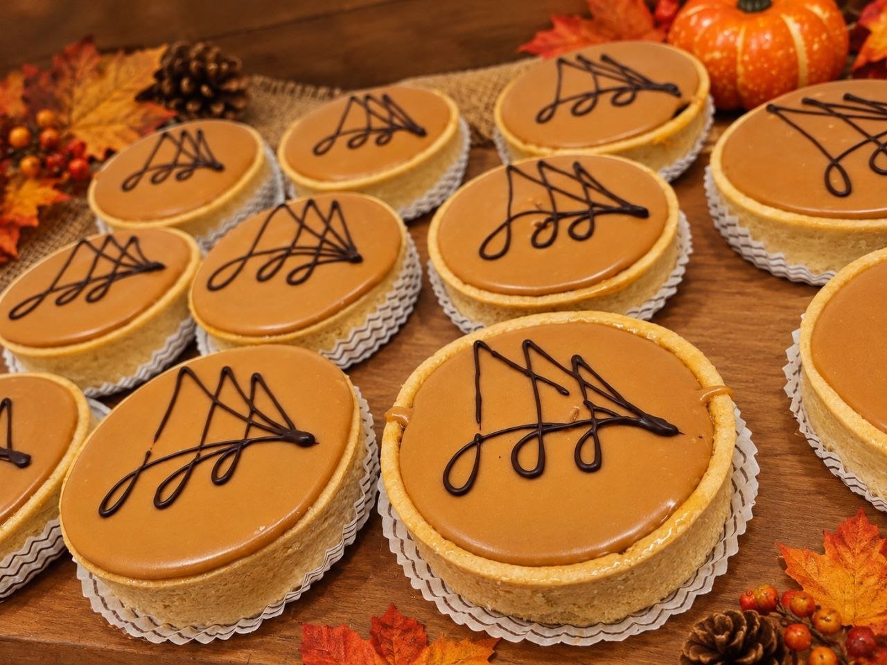 Caracs au caramel sur fond de pâte sablée, décorées d'un filet de chocolat, posées sur une planche en bois entourée de feuilles d'automne, de pommes de pin et d'une citrouille